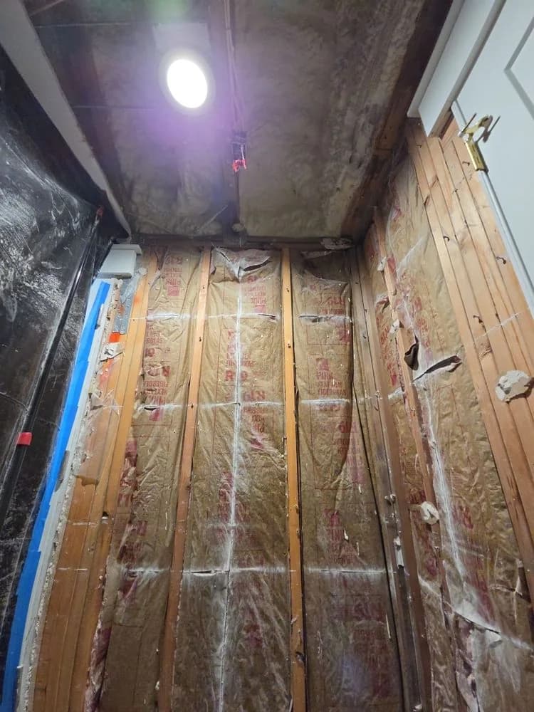 Wall opened up to the studs below a deck, with plastic sheeting