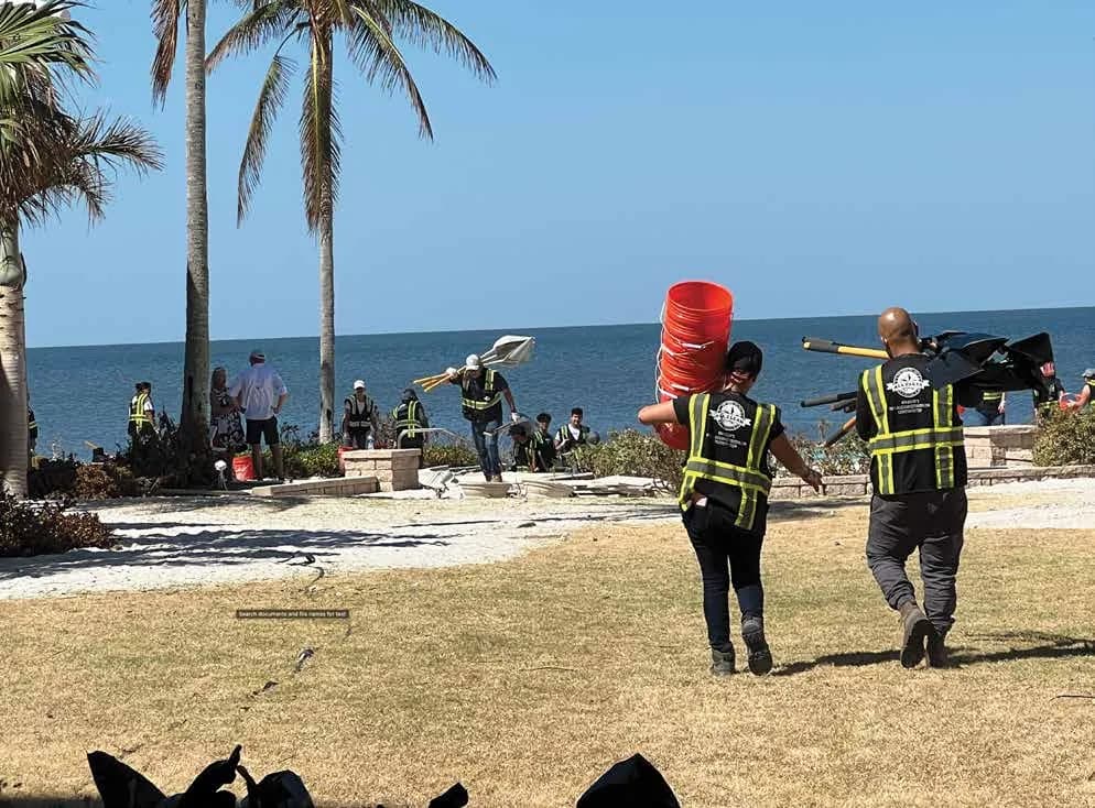 ALL CLEAR crew in branded safety vests carrying buckets and tools on a storm-hit waterfront