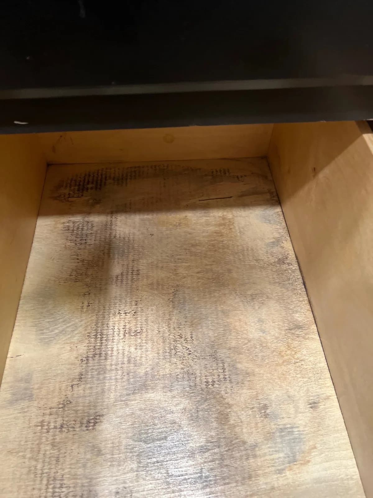 Looking down into an open wooden drawer. Its bottom panel has gray and brown mold streaks.