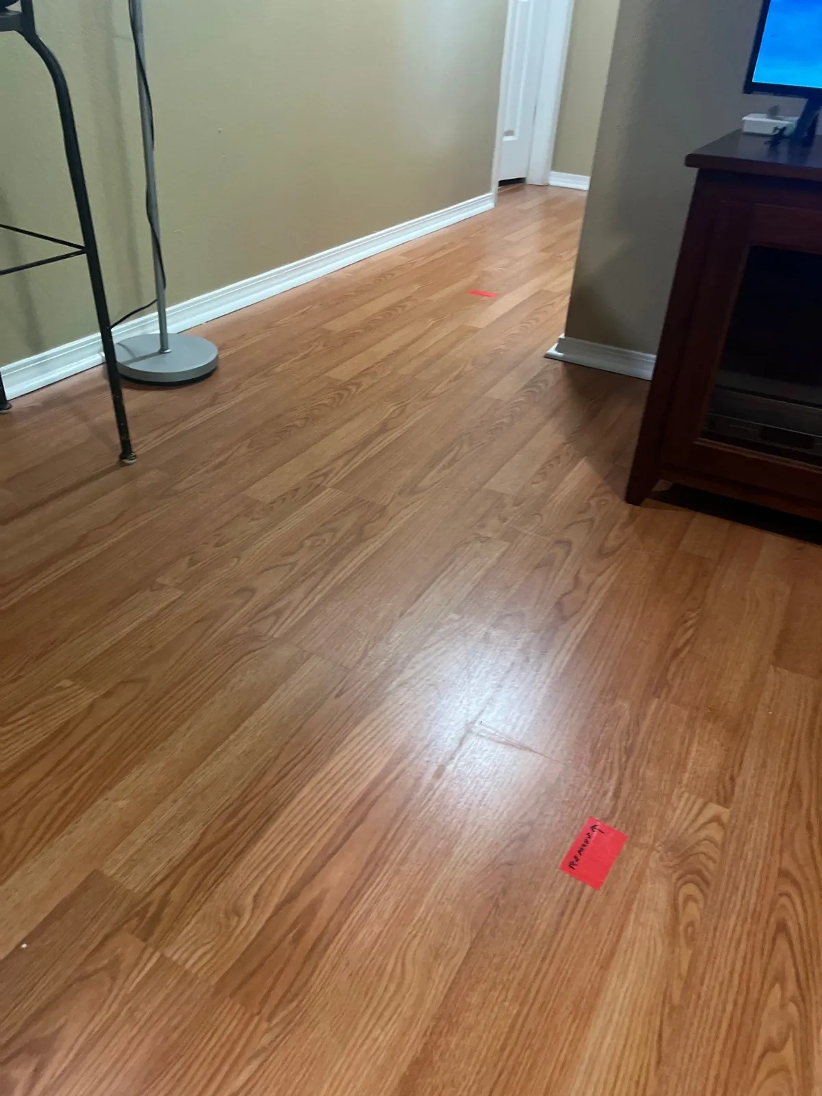 Wood-look laminate floor along a beige wall with white baseboard, with small red markers placed on the floor.