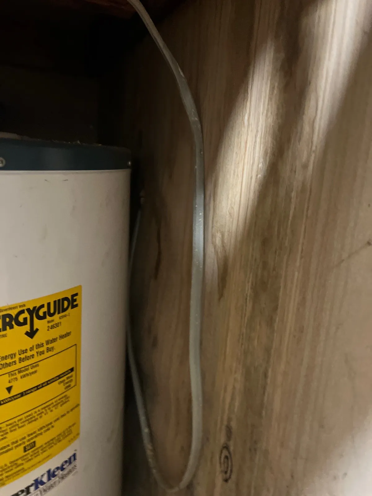 A narrow closet with a white water heater on the left and stained, discolored drywall on the right, with a gray cable running down the wall.