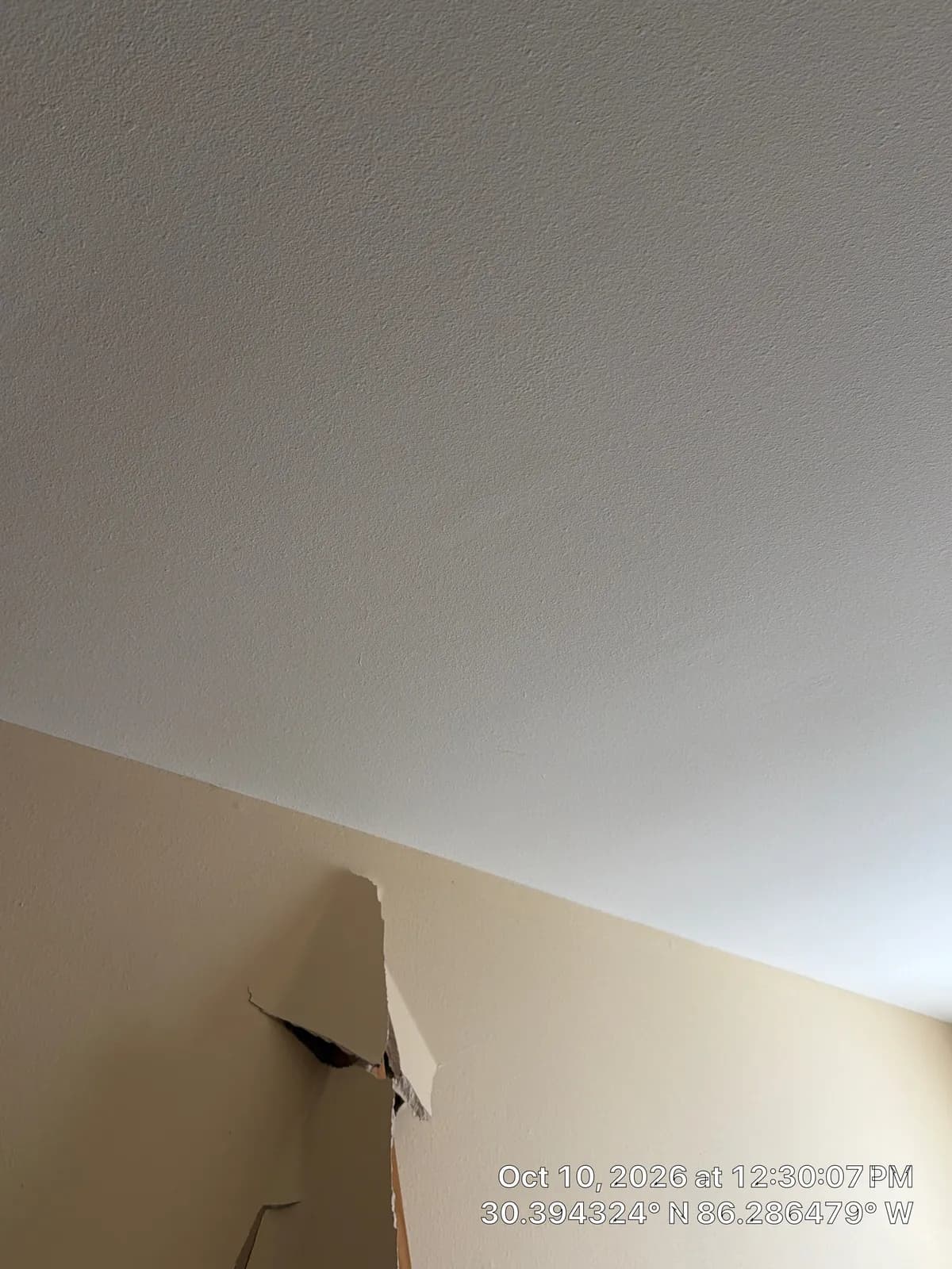 Textured white ceiling over a beige wall. Near the corner, a piece of drywall is torn and hanging loose.