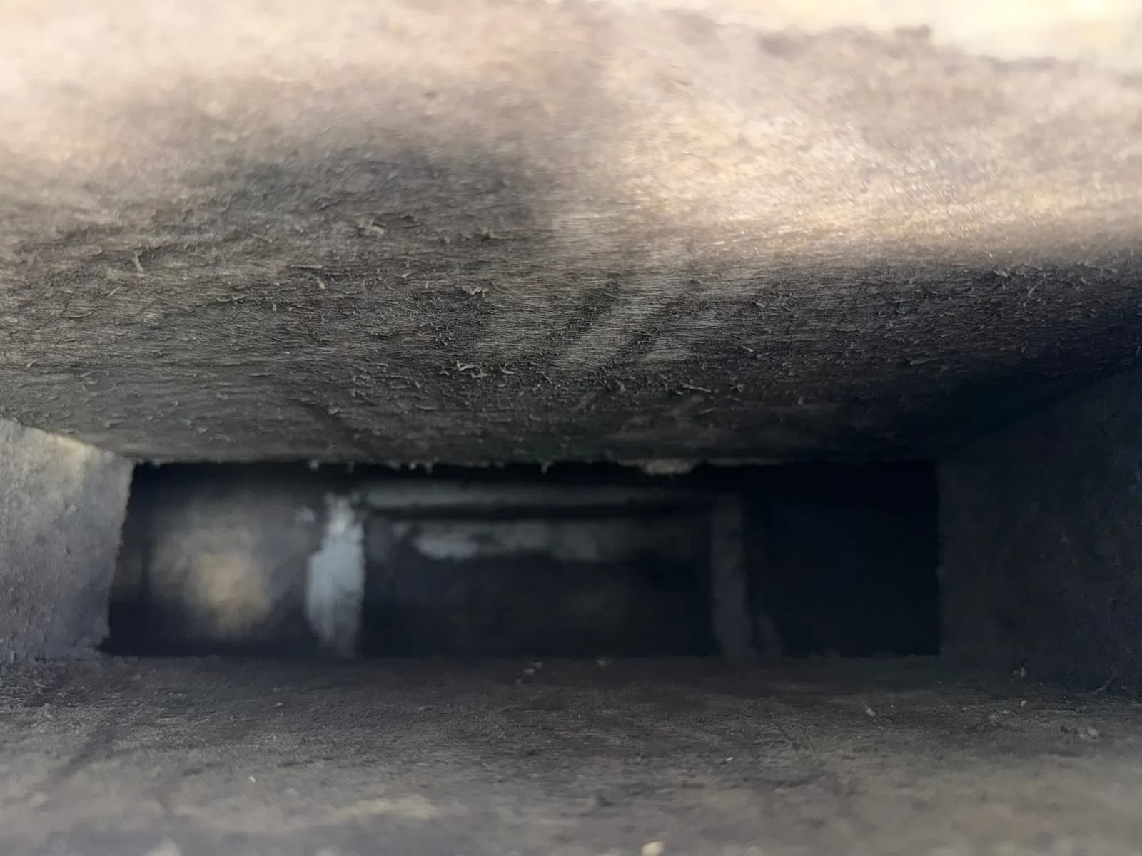 View down the inside of a rectangular duct with fibrous gray walls and dark staining.
