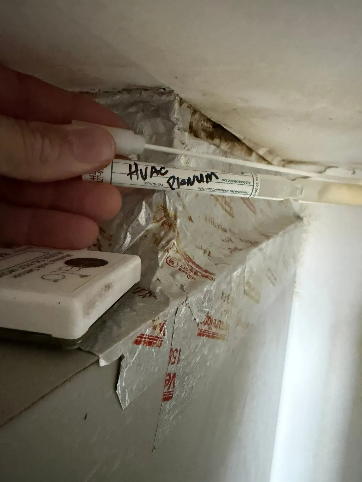 Gloved hand holding a swab tube labeled HVAC Plenum near a foil-taped duct joint.
