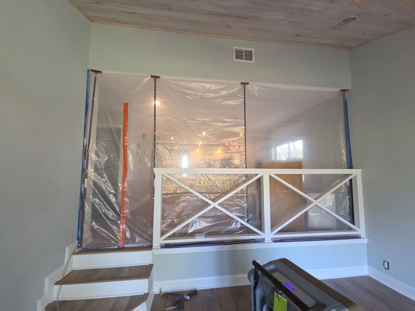 Clear plastic sheeting with zipper doors stretched floor to ceiling behind a white railing at the top of short steps.