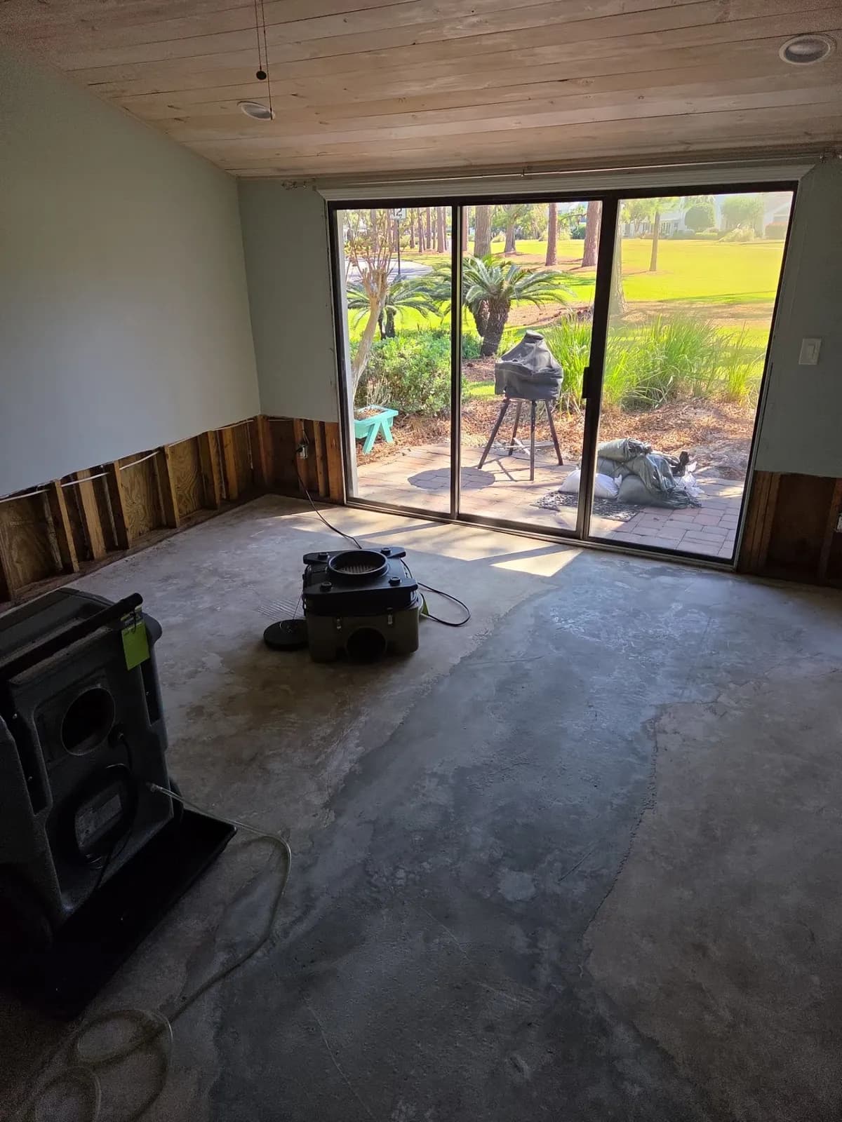 Room with bare concrete floor, lower walls cut open around the edges, and drying machines in front of sliding glass doors to a patio.